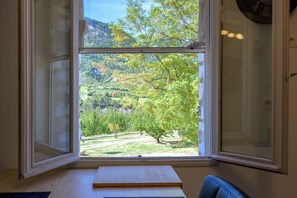 A room with a large window offering a view of a green landscape with trees and a hilly background.