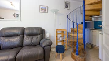A living room with a leather sofa, a lamp, and a staircase with blue railings leading to a kitchen area.