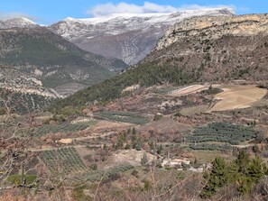 Paisatge montanyós amb una vall, un petit assentament i cims nevats al fons.
