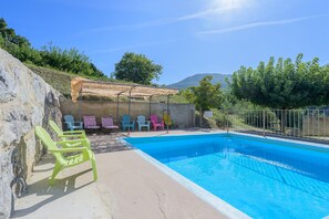 Una piscina amb una superfície d'aigua transparent i blava, envoltada per un solàrium de formigó. Hi ha cadires de plàstic de colors disposades al voltant de la piscina.