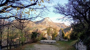 Un sendero de grava conduce a una estructura de piedra con diseño circular, rodeada de árboles y una montaña al fondo.