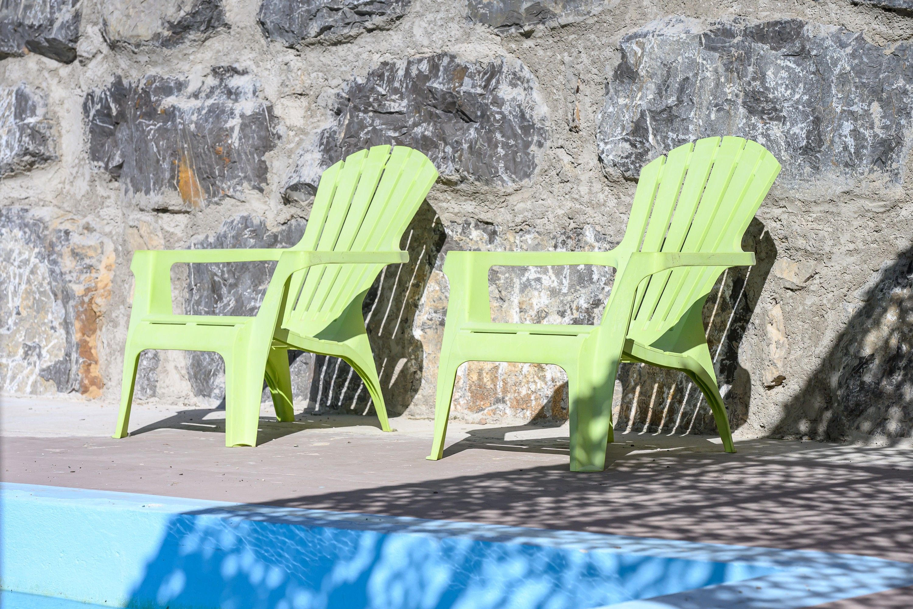 Dos sillas Adirondack verdes junto a una piscina con un muro de roca al fondo.