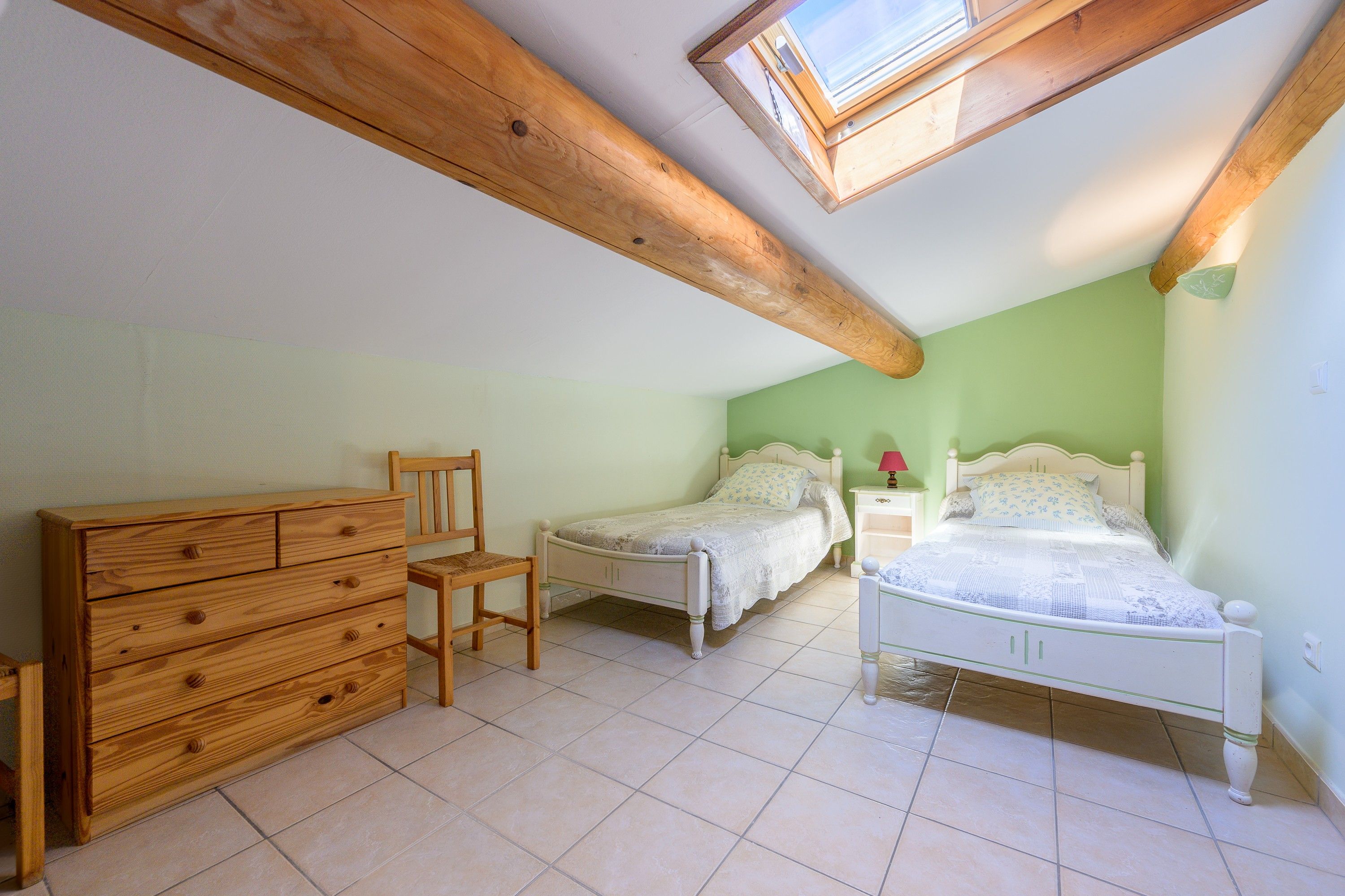 A bedroom with two single beds, a wooden dresser, a chair, and a skylight.