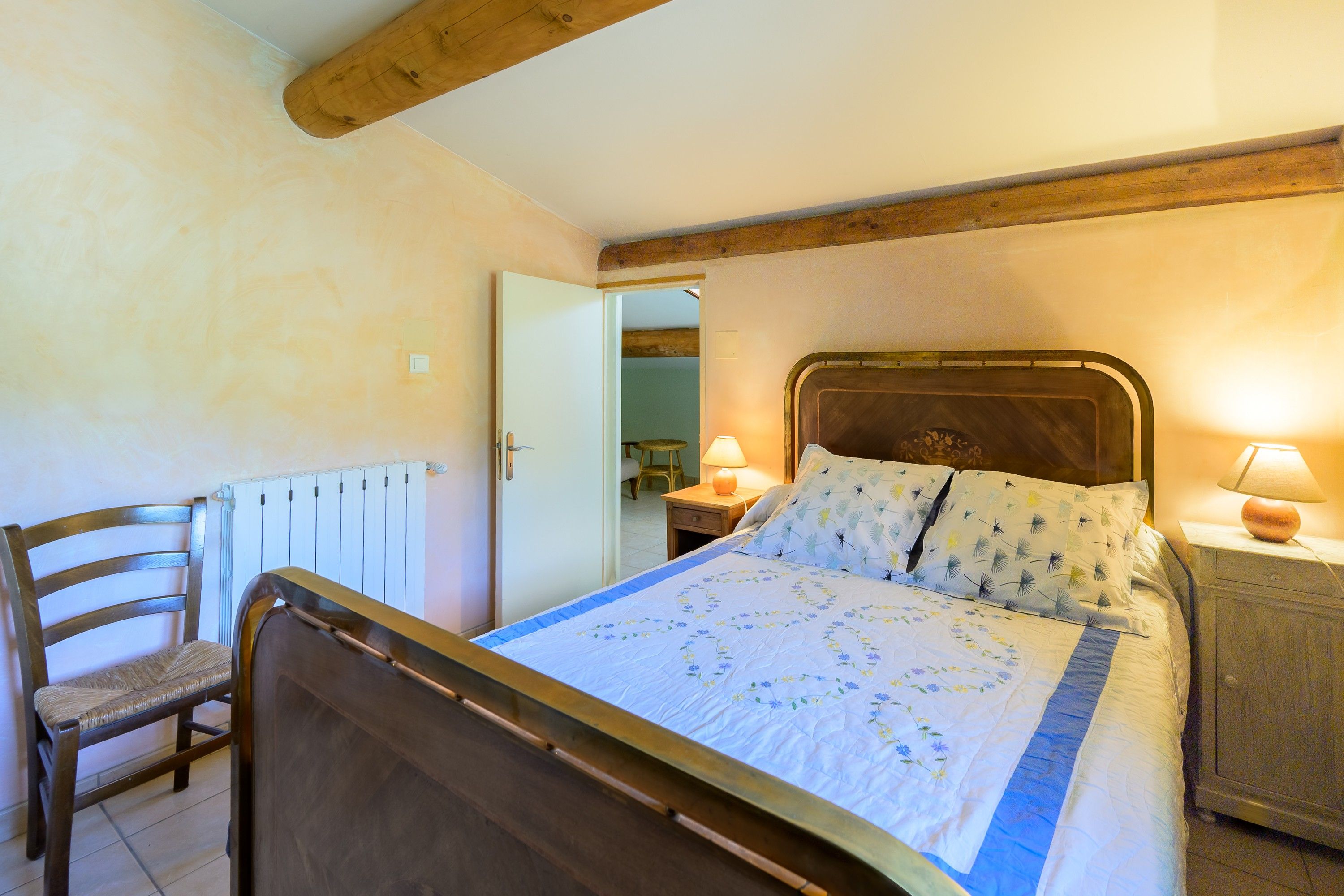Une chambre à coucher avec un lit en bois, une chaise, une table de chevet avec une lampe et un radiateur.