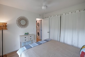 A bedroom with a bed, a bedside table, a lamp, a mirror, and a laundry area. - Elegant and spacious, walk to shopping, dining, Anini beach (Princeville)