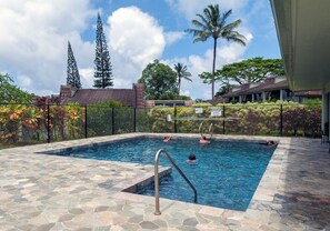 Ein Swimmingpool mit Steinplatten, umgeben von einem Zaun, Palmen und einem Gebäude mit einem Ziegeldach.