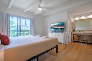A bedroom with a bed, a television, a bathroom with a mirror, and a balcony with curtains. - Elegant and spacious, walk to shopping, dining, Anini beach (Princeville)