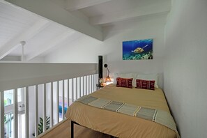 A bedroom with a bed, a painting of a sea turtle, a nightstand with a lamp, and a balcony with a railing. - Elegant and spacious, walk to shopping, dining, Anini beach (Princeville)