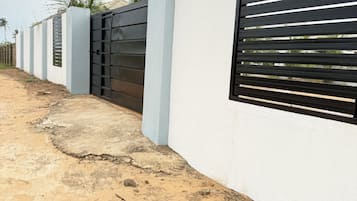 Un edificio moderno con fachada de concreto, entrada protegida por una reja y un camino pavimentado.