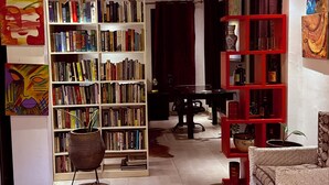 A spacious living room with a large bookshelf, a red shelving unit, and a wicker sofa. - Beachside Studio with a Curated Library (P32W+99C Prampram)
