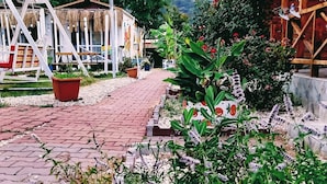 A rustic outdoor area with a wooden structure, a swing set, and a paved walkway leading to a mountain backdrop. - zeyos lodge (kumluca)