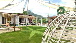 A grassy outdoor area with a hammock, a table, and a thatched-roof structure. - zeyos lodge (kumluca)
