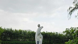 A sculpture of a human figure on a pedestal in a landscaped garden.
