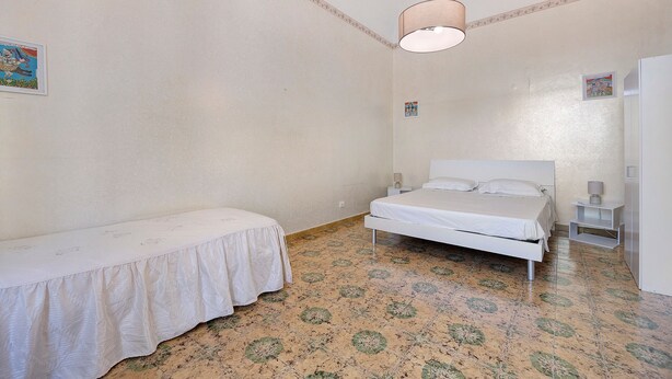 Una stanza piccola e modesta con un letto, un comodino, una lampada e un frigorifero.