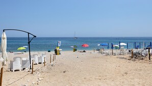 Una spiaggia con file di sedie a sdraio bianche e ombrelloni, cielo sereno e mare sullo sfondo.