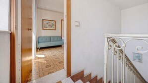 Un corridoio con un divano blu, una scala con balaustre bianche e piastrelle decorative.