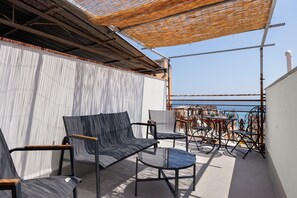 An outdoor seating area with a table and chairs, a view of the sea, and a covered section with a thatched roof. - Terrazze Arenella Guest House: Sea View, Wi-Fi, Air Conditioning (Palermo)