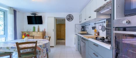 A modern kitchen with a flat-screen TV, wooden cabinets, and a dining area with a table and chairs.