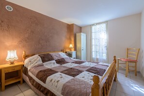 Ein Schlafzimmer mit Bett, Nachttisch, Lampe, Kleiderschrank, Stuhl und einem Fenster mit Vorhängen.