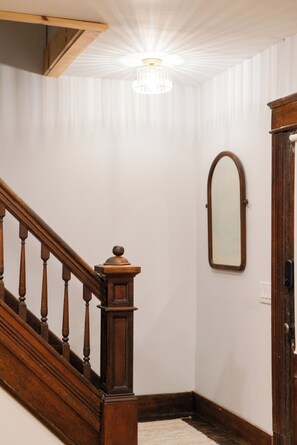 Un escalier avec des balustrades en bois et une main courante, menant à une pièce aux murs blancs et dotée d’un luminaire au plafond.