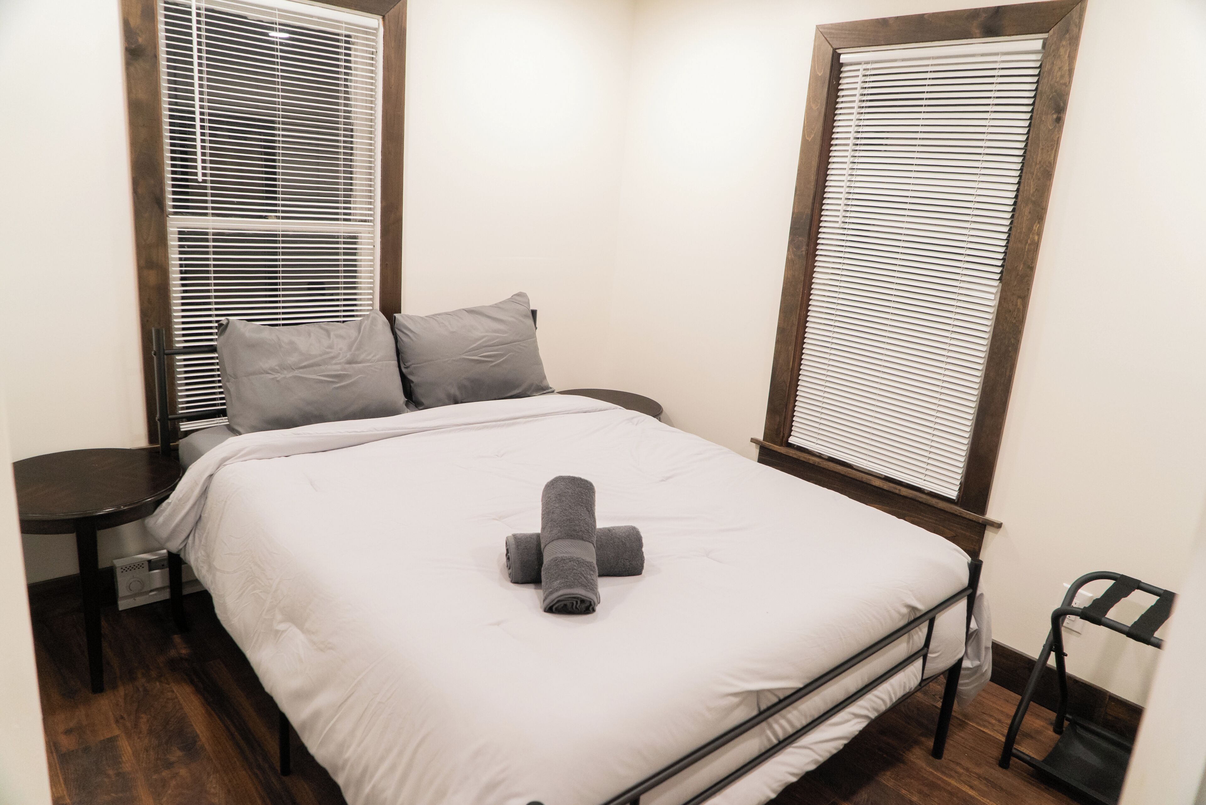 A small, neatly arranged bedroom with a bed, two pillows, a bedside table, and a chair.