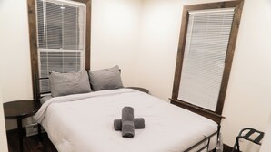 Quarto pequeno e bem organizado com uma cama, duas almofadas, mesa de cabeceira e uma cadeira.
