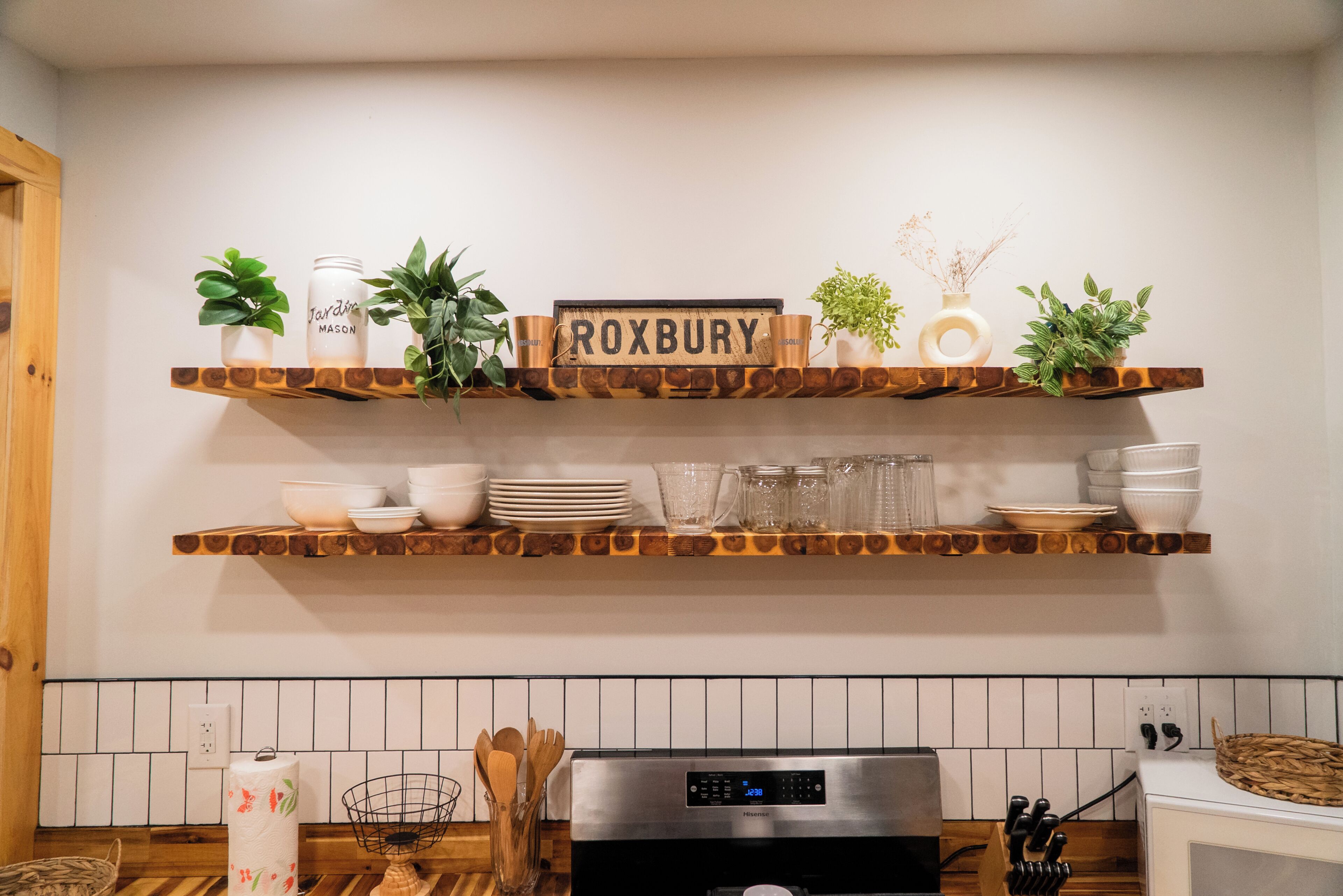 Una cocina con estantes de madera que exhiben utensilios de cocina y plantas, un refrigerador Hisense y un salpicadero de azulejos.