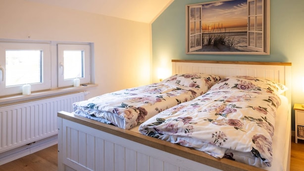 Ein Schlafzimmer mit einem Bett, zwei Fenstern, einer Heizung und einem Bild an der Wand.