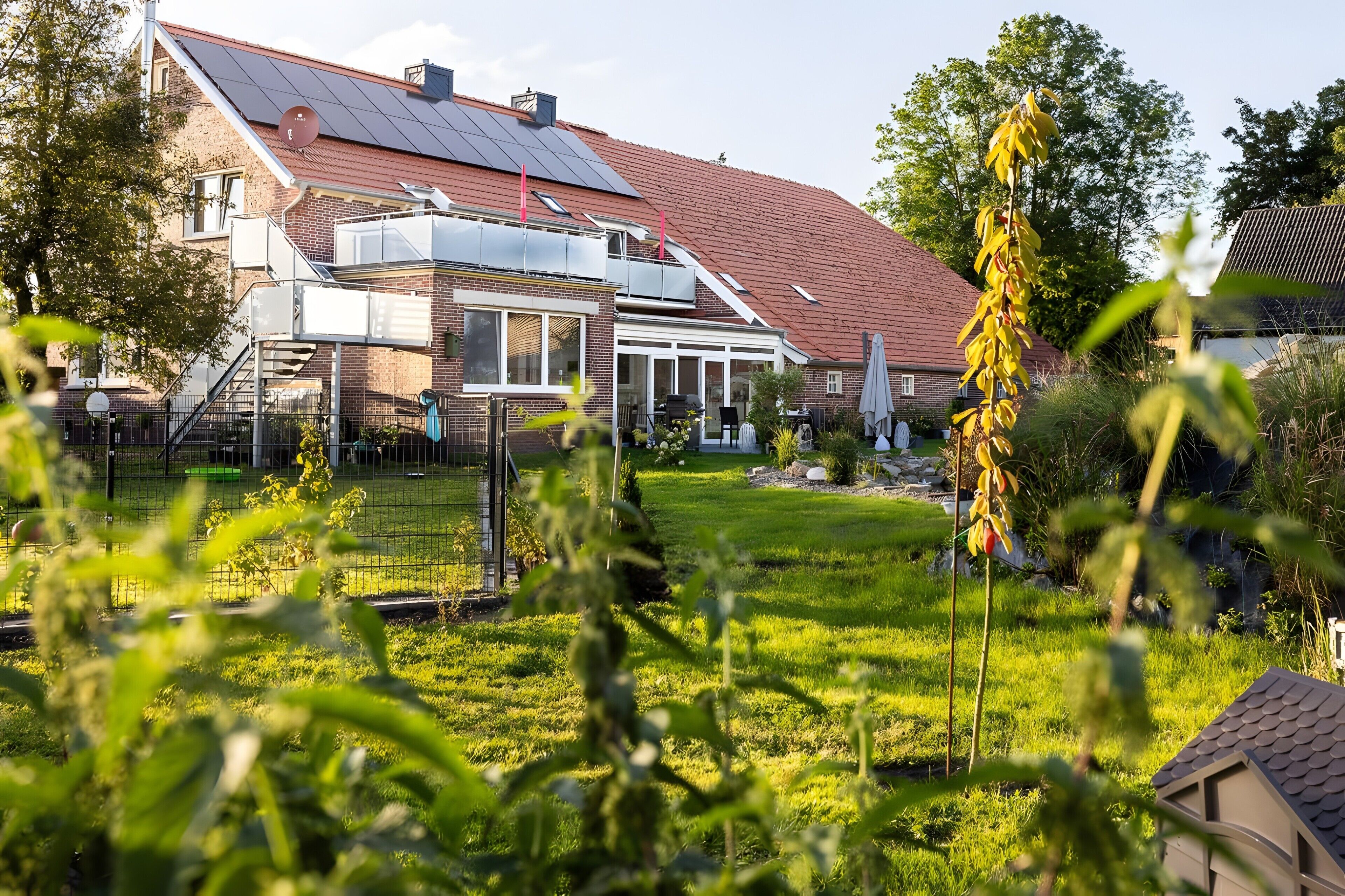 Een woonhuis met een schuin dak, zonnepanelen, een omheinde tuin en een tuin.