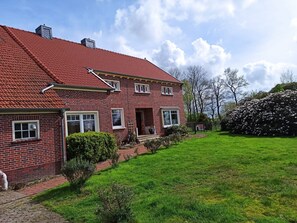 A two-story brick house with a red-tiled roof, a front porch, and a well-maintained lawn. - Apartment 'Kleines Mehr' with Wi-Fi (Südbrookmerland)