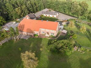 A large building with a red roof, surrounded by a well-maintained lawn and trees. - Apartment 'Großes Mehr' with Wi-Fi (Südbrookmerland)