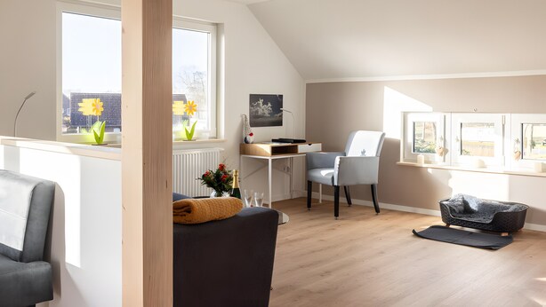 Ein modernes Wohnzimmer mit einer Couch, einem Sessel, einem Schreibtisch und Blick ins Freie.