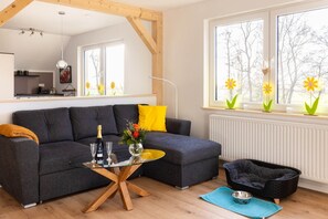 Uma sala de estar moderna com um sofá cinzento, uma mesa de centro de vidro e uma caminha preta para animais de estimação.