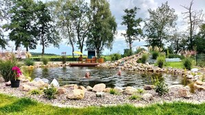 Ein Teich mit einer Holzterrasse und Sitzgelegenheit, umgeben von Steinen und Grünpflanzen.
