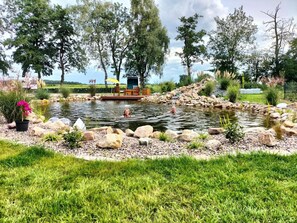 A pond with a wooden deck and seating area, surrounded by rocks and greenery. - Apartment 'Großes Mehr' with Wi-Fi (Südbrookmerland)