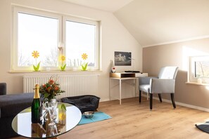 A modern living room with a glass table, a sofa, a chair, a radiator, and a desk with a computer. - Apartment 'Großes Mehr' with Wi-Fi (Südbrookmerland)