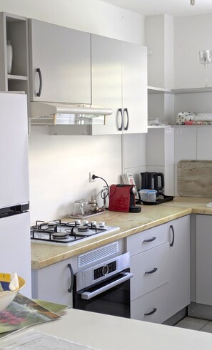 A modern kitchen with white cabinets, a gas stove, a coffee maker, and a wooden cutting board. - Apartment with a breathtaking view of Trinity Bay (La Trinité)