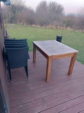 Eine Holzterrasse mit Tisch und Stühlen, umgeben von einem Rasen und Bäumen.
