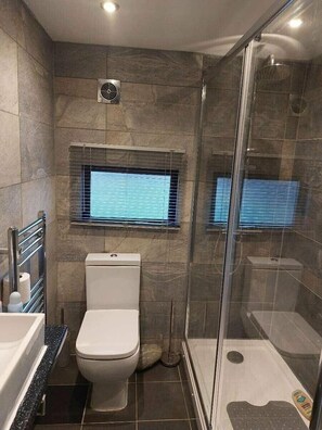 Ein Badezimmer mit Toilette, Duschkabine und Fenster mit Jalousien.