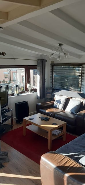 A living room with a sofa, a coffee table, a TV, and a window with blinds.