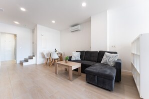 Ein modernes Wohnzimmer mit einer Couch, einem Hocker und einem Esstisch mit Stühlen.