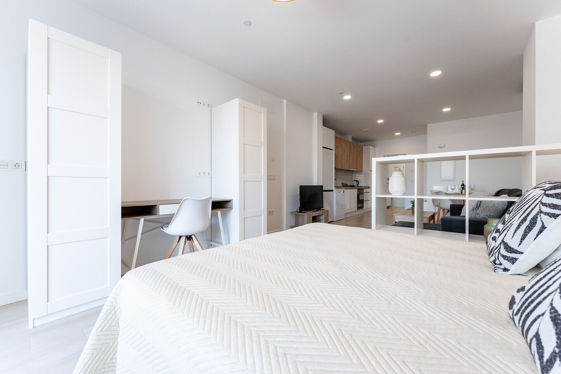 Une chambre moderne avec un grand lit, un bureau et, au fond, un coin cuisine.