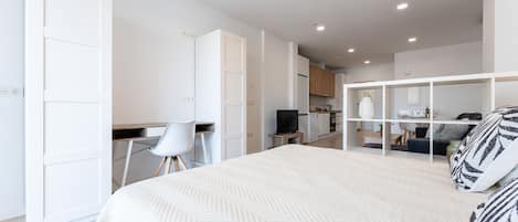Un dormitorio moderno con una cama grande, un escritorio y una kitchenette al fondo.