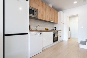 Eine moderne Küche mit weißen Schränken, einer Mikrowelle, einer Kaffeemaschine und einer Obstschale auf der Arbeitsplatte.