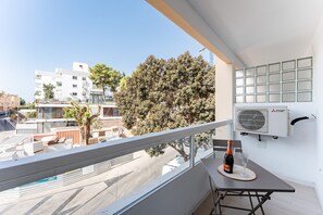 A balcony with a table, a bottle, and a glass, overlooking a street with buildings and trees. - MalagaSuite Urban Beach A (Torremolinos)