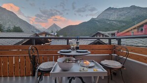 Una mesa de comedor con una copa de vino blanco, una vela y un bol de comida en un balcón con vistas a la montaña.
