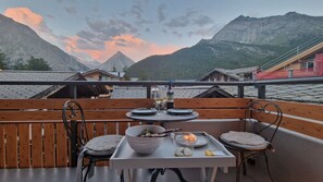 Ein Esstisch mit einem Weinglas, einer Kerze und einer Schüssel Essen auf einem Balkon mit Bergblick.