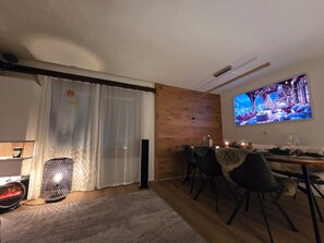 A cozy living room with a fireplace, a dining area with a table and chairs, and a large TV mounted on the wall. - High-quality, stylish furnishings | Mountain views (Saas-Fee)