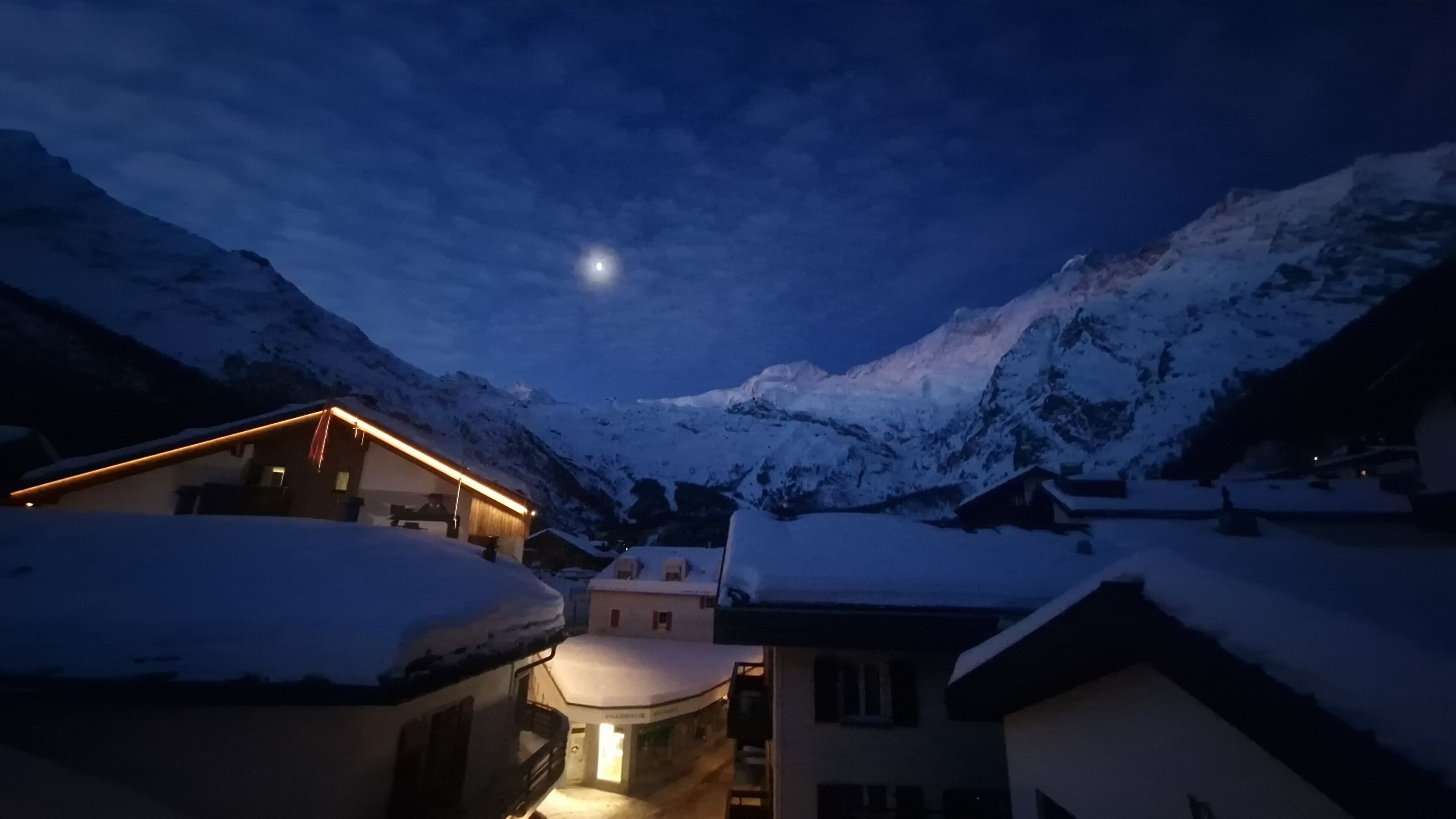 Un pueblo en la montaña cubierto de nieve, de noche, con una luna visible.