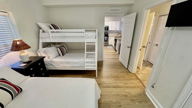 Un dormitorio compacto con camas literas, una mesita de noche con lámpara y vistas al área de cocina contigua.